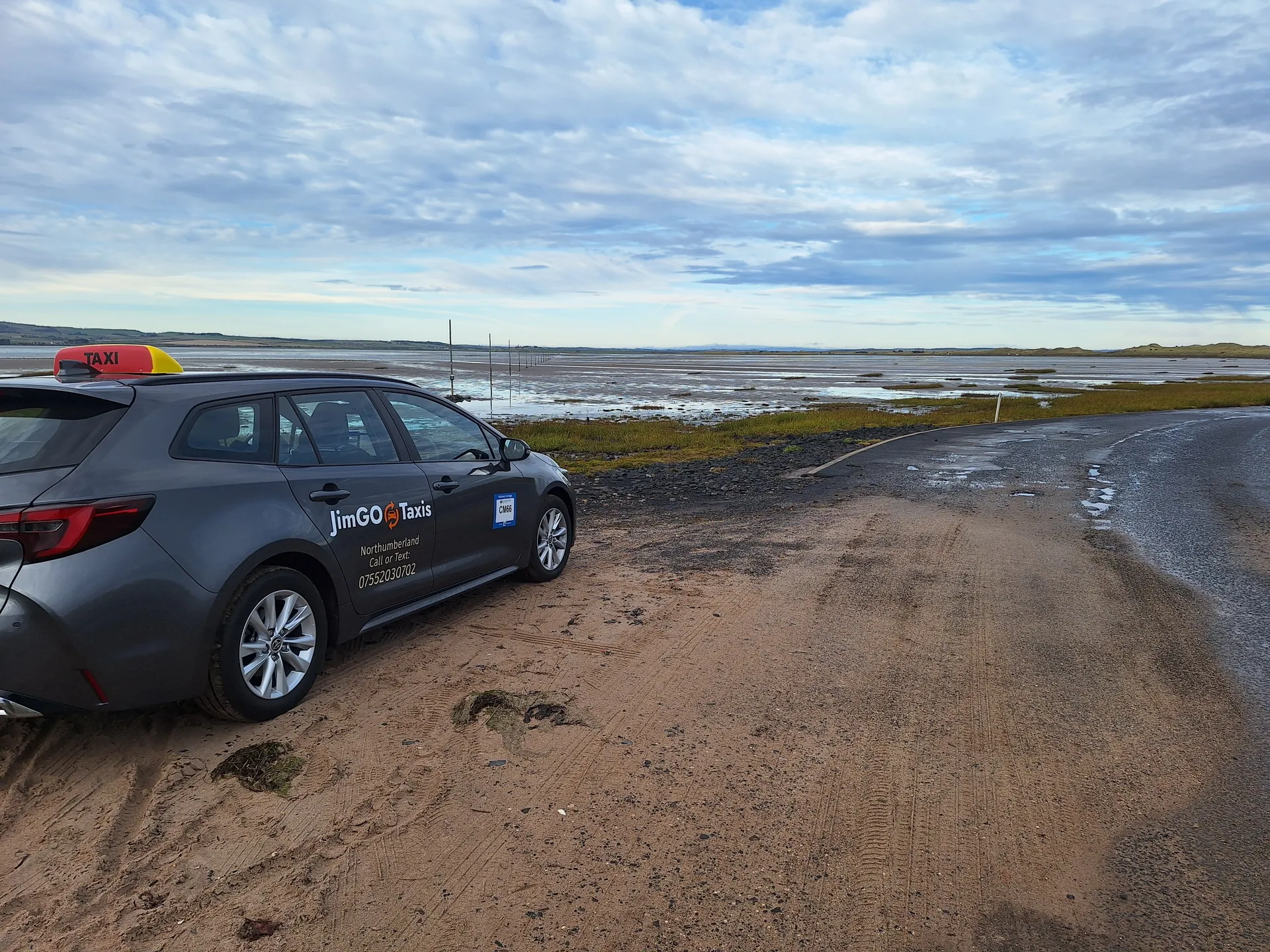 The JimGO taxi on the Holy Island causeway with the tidal flats behind it