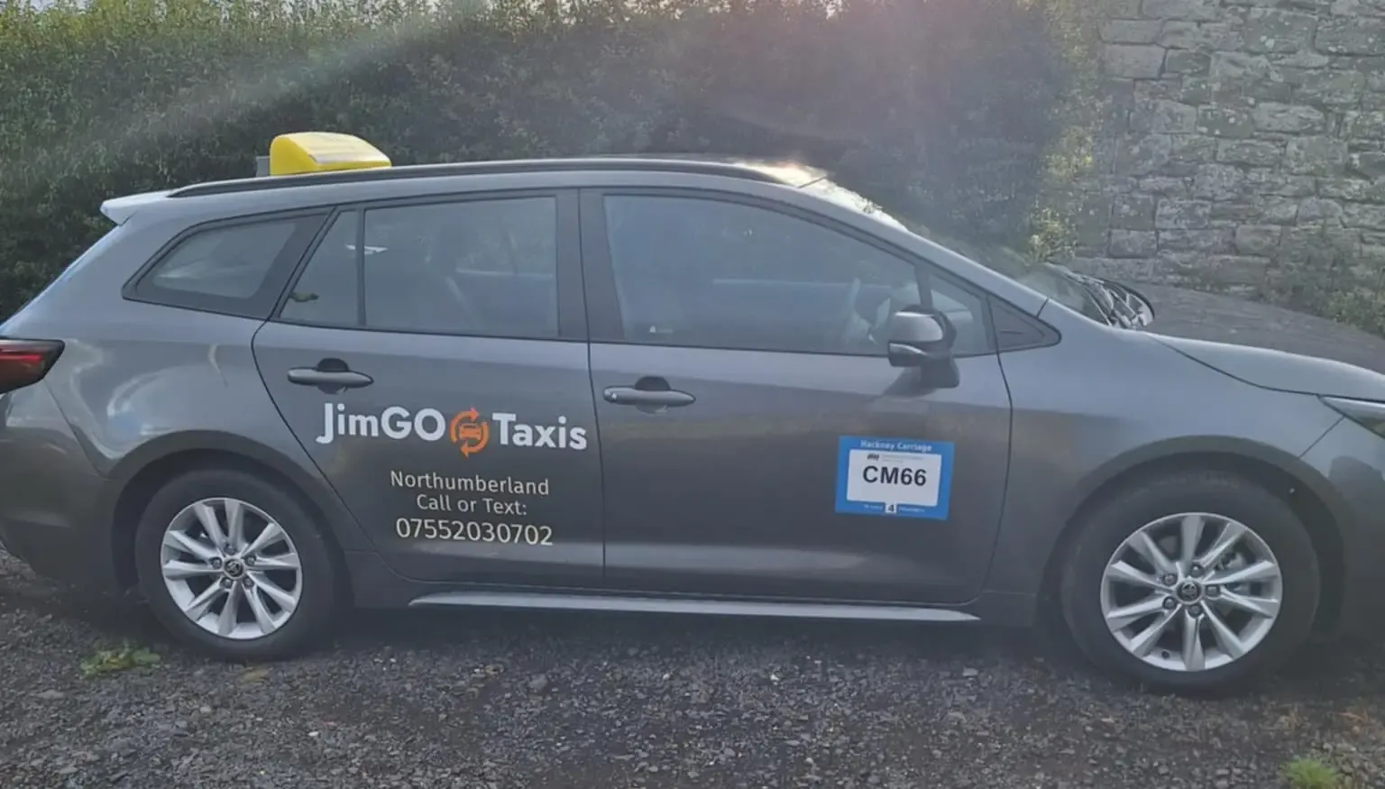 The JimGO taxi beside a stone wall in the evening sun, its council licence plate on the front door