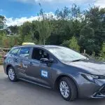 Grey Toyota Corolla Hybrid taxi featuring a sign that says "JimGO Taxis" ready for passengers.